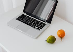 A modern laptop beside fresh fruit on a sleek, minimalist desk setting.